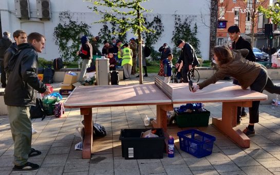 homeless men play ping pong next to a soup kitchen