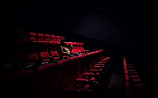 A person sat in a cinema on a red seat watching a film with nobody else in the room with them