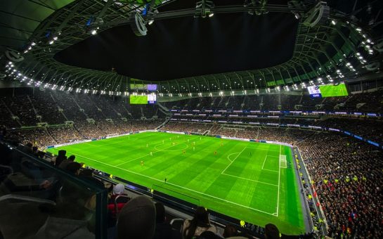 An image of fans in a stadium watching a football match at nighttime