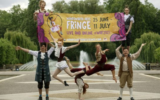A troop of performers hold a banner advertising the fringe.