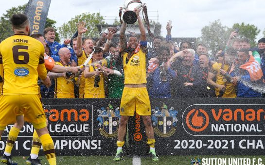 Sutton FC celebrate- holding cup and celebrating with fans in the background