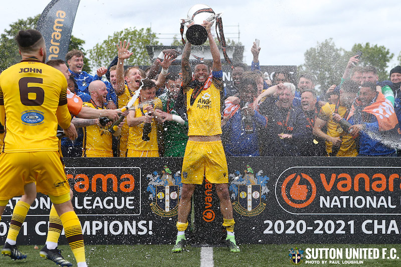 Sutton FC celebrate- holding cup and celebrating with fans in the background