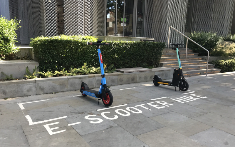A picture of e-scooters parked in their designated bay which is on the pavement and marked with a white line. The photo was taken in Hammersmith