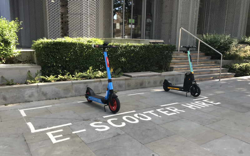 A picture of e-scooters parked in their designated bay which is on the pavement and marked with a white line. The photo was taken in Hammersmith