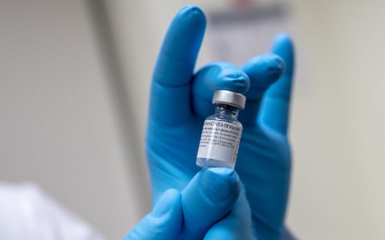 a pair of blue-gloved hands holding a vial with the vaccine