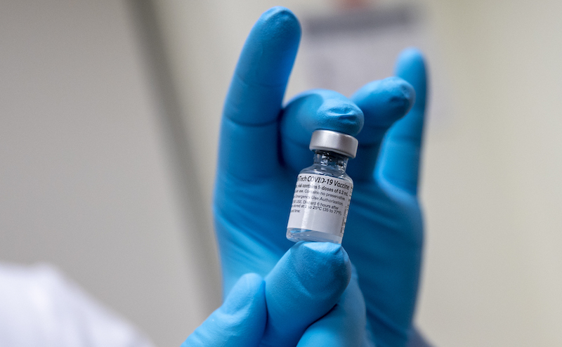 a pair of blue-gloved hands holding a vial with the vaccine