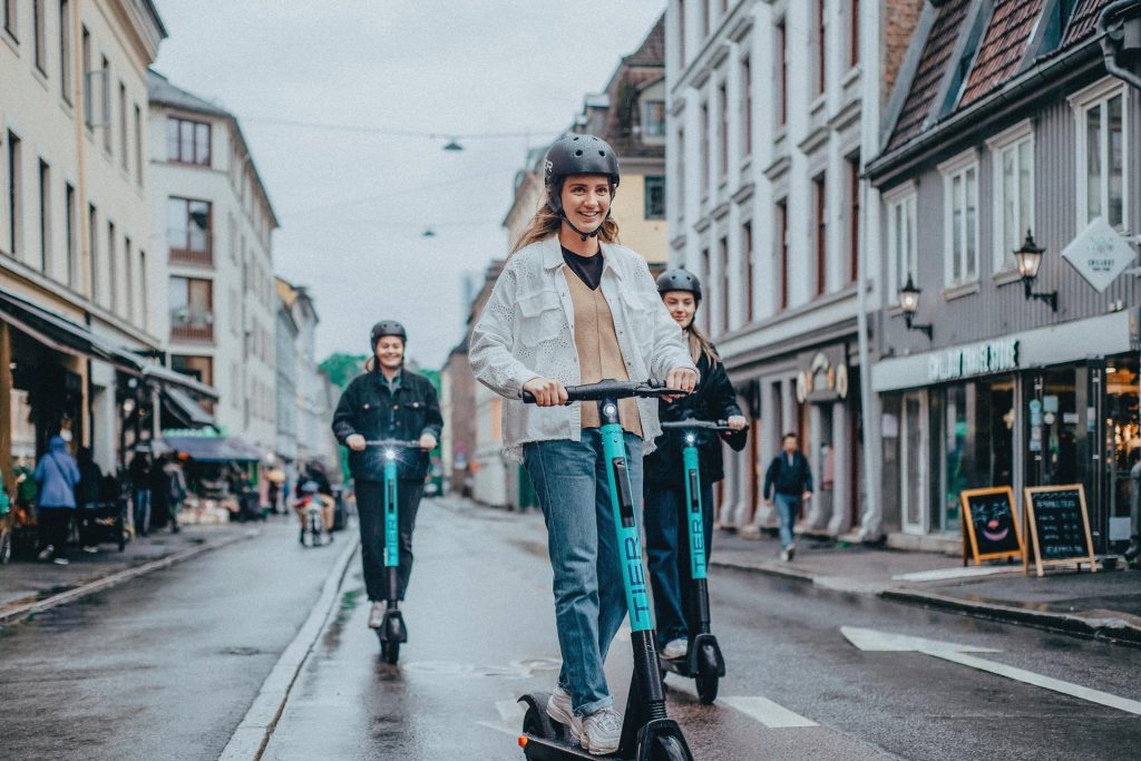 Smiling young people try out TIER e-scooters wearing helmets and scooting in a cycle lane in this promotional picture from Tier