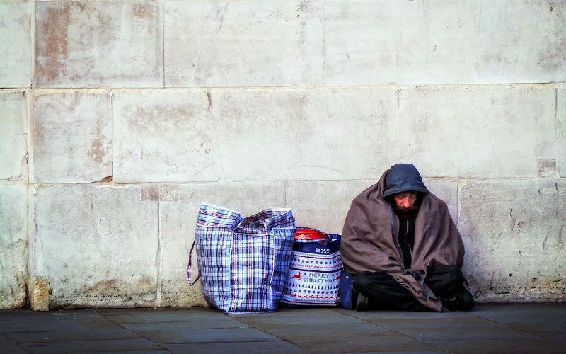 homeless man sitting up against a wall