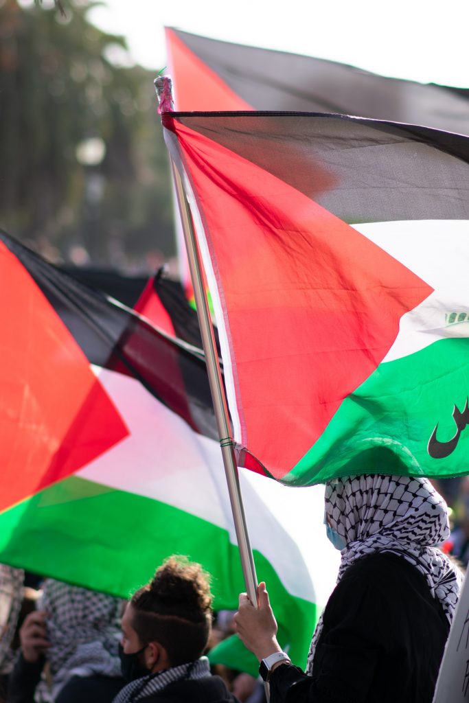 Protesters for the Palestinian cause waving the flag, many of whom wear traditional 'khafiya' headscarves. Photo by Patrick Perkins on Unsplash