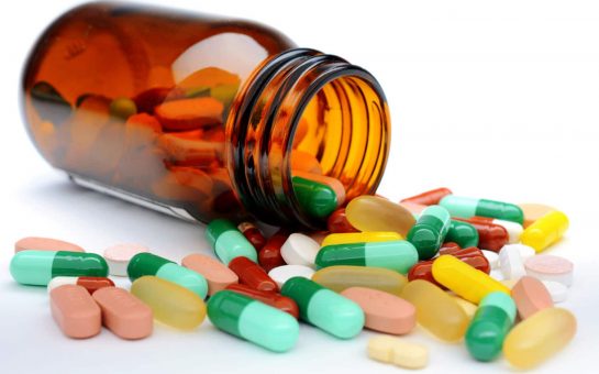 Multicoloured pills spilling out of a bottle onto a white table