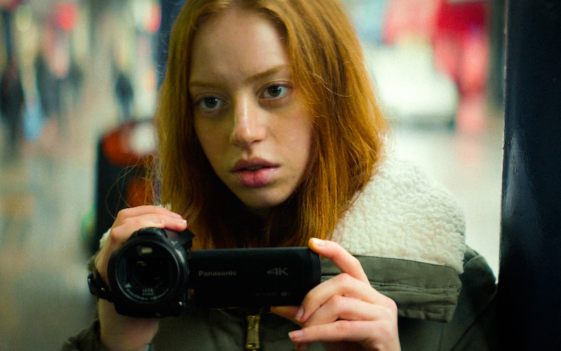 Lily Newmark as Leah, holding a video camera in scene from A Brixton Tale