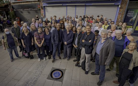 Supporters crowd around a rainbow plaque commerating "My Beautiful Laundrette"