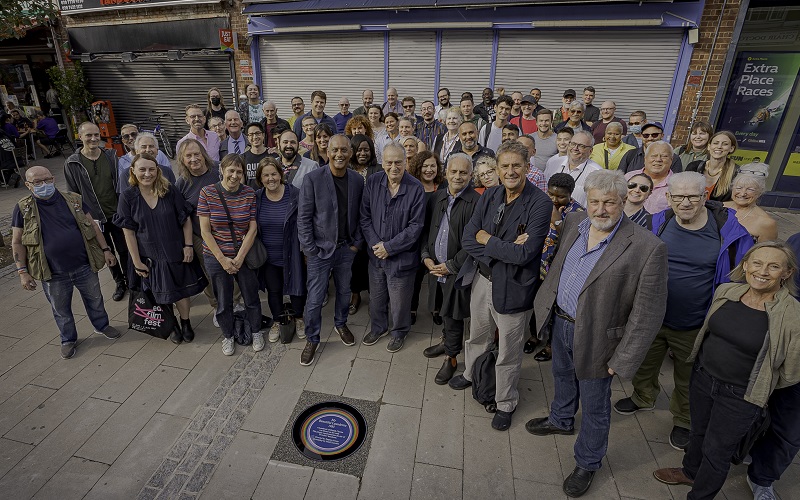 Supporters crowd around a rainbow plaque commerating "My Beautiful Laundrette"