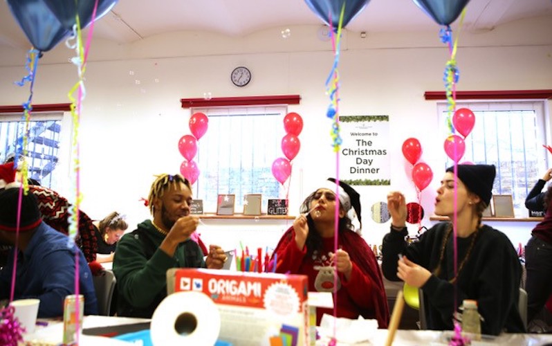 Three young care leavers blow bubbles sat around a table at a Richmond Christmas Day Dinner party