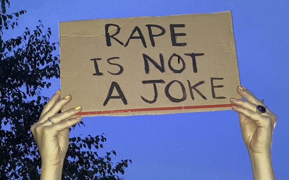 Hands holding up a protest sign saying "Rape is not a joke"