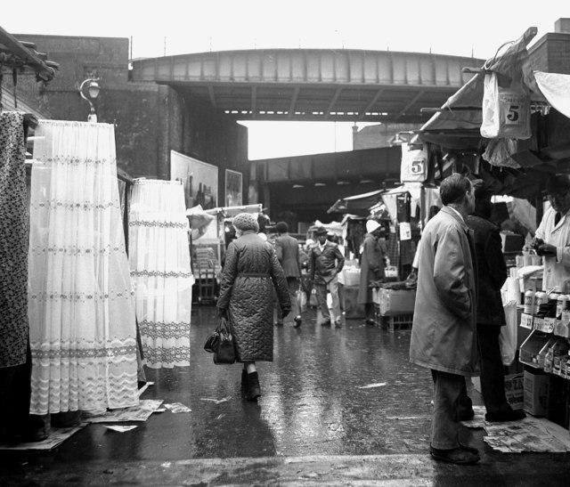 Brixton market in 1981 with people walking through it. 