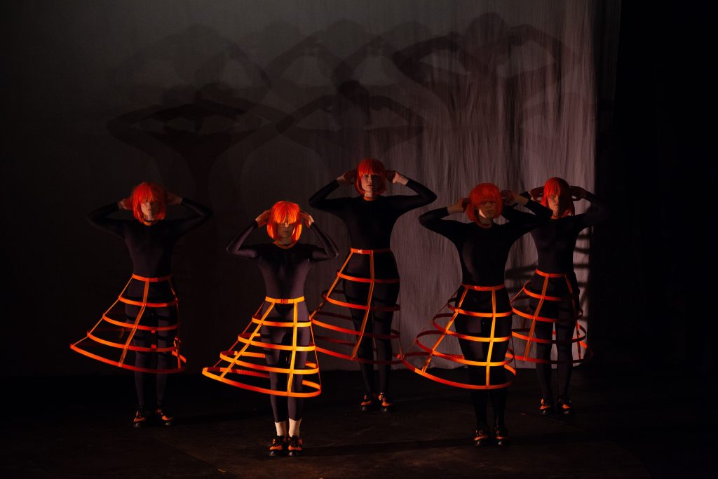 Figs in wigs performers on stage in orange wigs and skirts