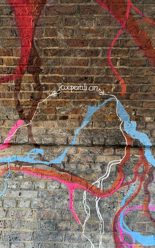 A close-up of a section of the climate mural on which orange, pink, blue, and brown roots sprawl around the word "cooperation"