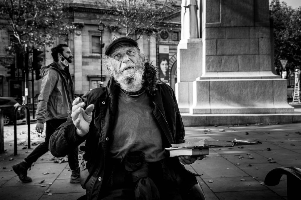 Homeless man holding books and looking at camera, by Photographer Anthony Dawton