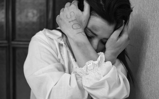Woman holding head in hands, with "stop" written on arm