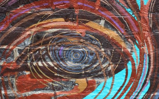 A close-up of a brick wall painted in bright pinks, blues and oranges to look like a knot in a tree trunk