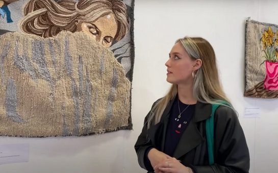 Artist Llinos Owen stands in front of her tapestry depicting herself in her bed during lockdown