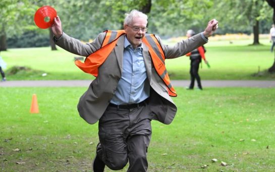 An elderly man in a high-vis vest finishes parkrun