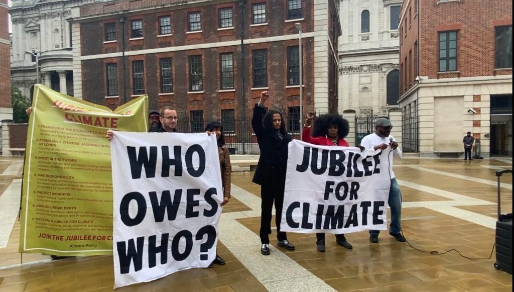 Africans Rising activists holding banners that say 'who owes who?' and 'jubilee for climate'.
