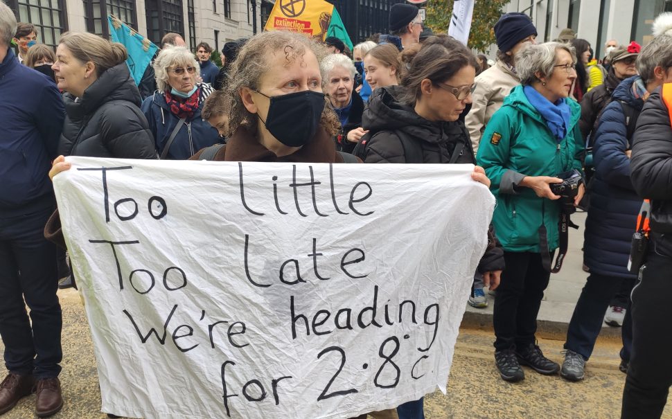 A woman holding a white piece of fabric, reading: "Too little, too late, we're heading for 2.8°C."