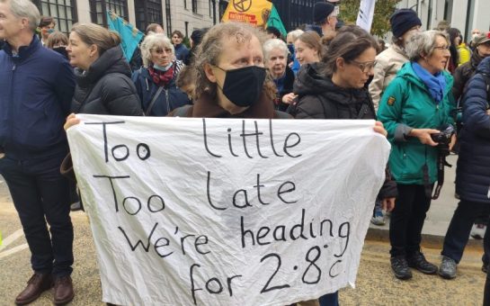A woman holding a white piece of fabric, reading: "Too little, too late, we're heading for 2.8°C."