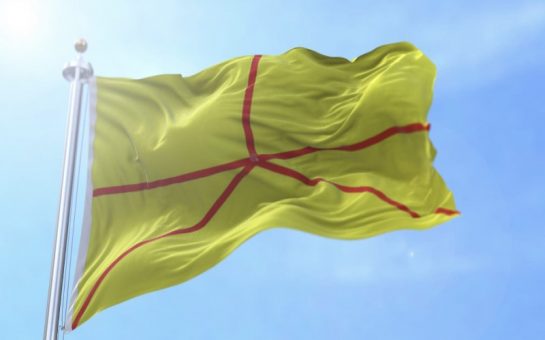 Flag of Austenasia, yellow background with red chevron, flying against a blue sky