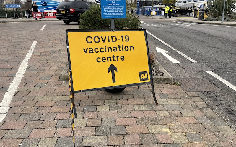Yellow sign saying "COVID-19 vaccination centre" with an arrow pointing ahead