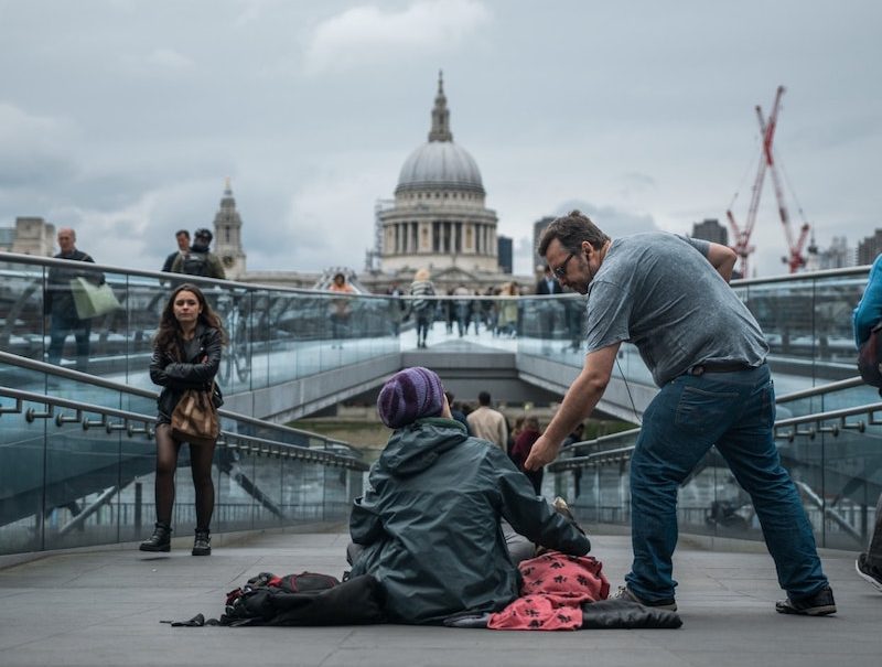 man handing homeless person money in london