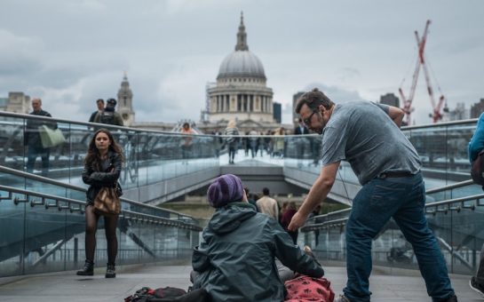 man handing homeless person money in london