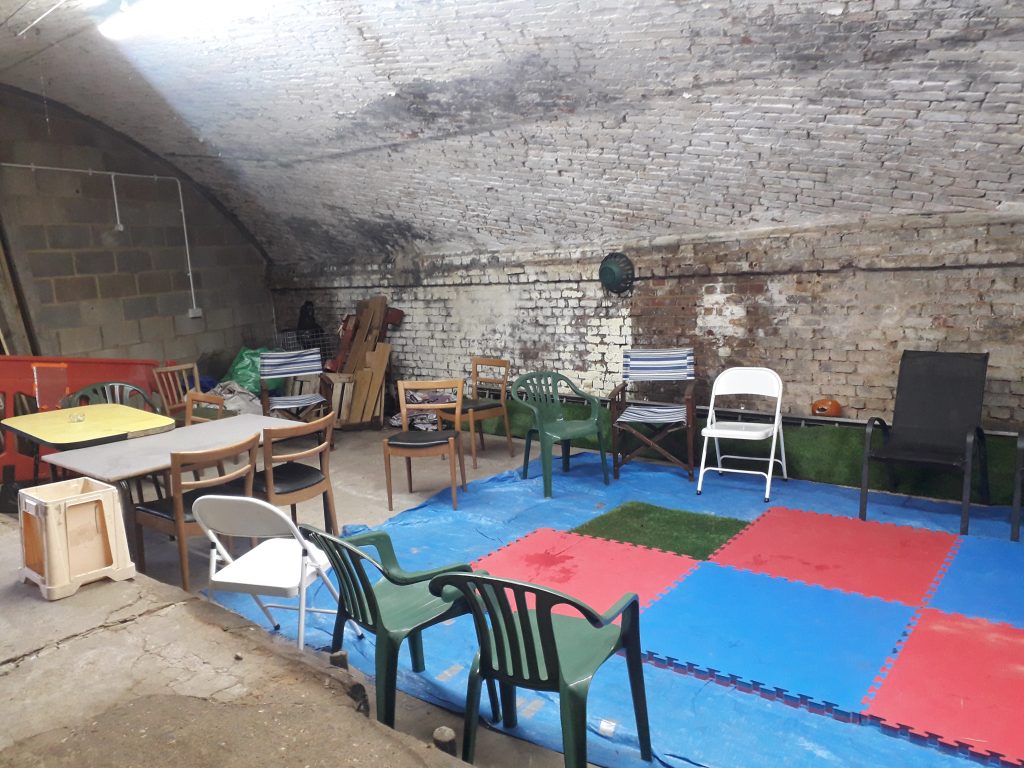 A large undergound room with a number of small tables and chairs grouped around the centre.