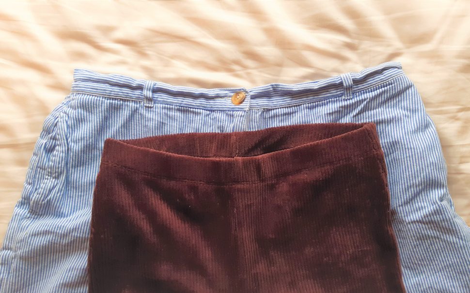A pair of trousers with a small waistband lying on top of a pair of shorts with a larger waistband