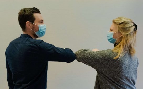 Two people wearing covid masks bump elbows in greeting