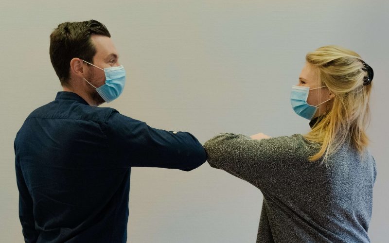 Man and Woman wearing face masks bump elbows in greeting