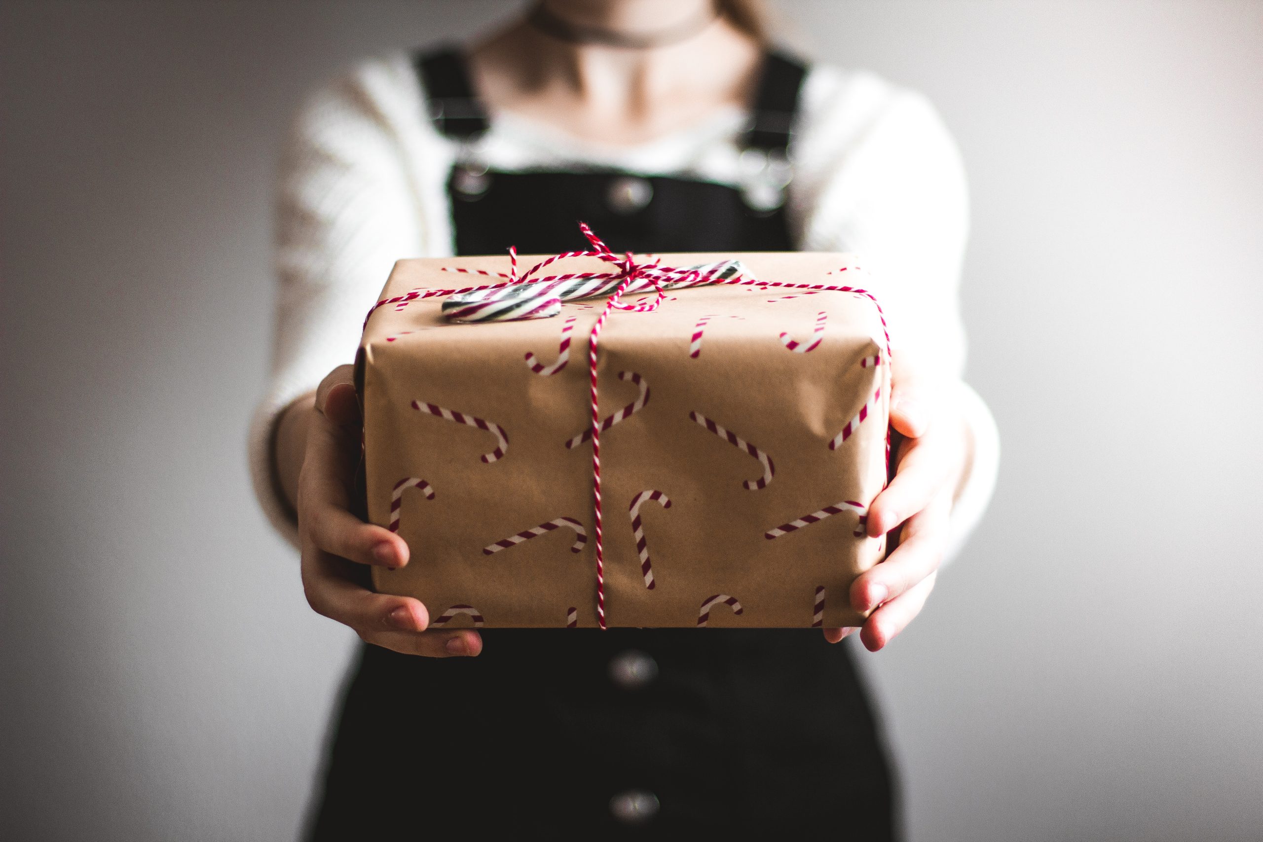 A woman holding out a present wrapped in brown wrapping paper with candy canes on it.