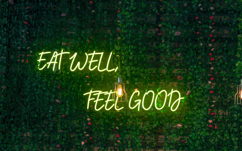 Green luminous sign 'Eat Well Feel Good' against foliage