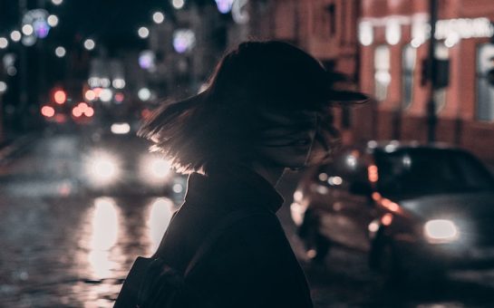 woman in black jacket carrying backpack with tousled hair walking on the street at night