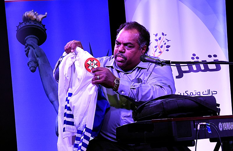 Black musician Daryl Davis holds up the robes of a Ku Klux Klan member on stage