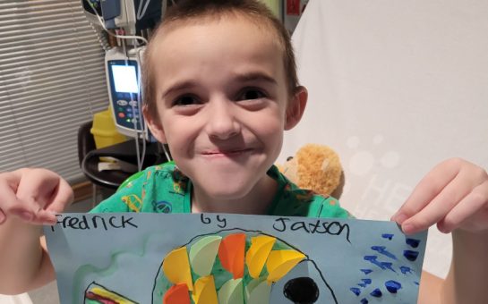 Young patient Jaxson smiles holding his artwork