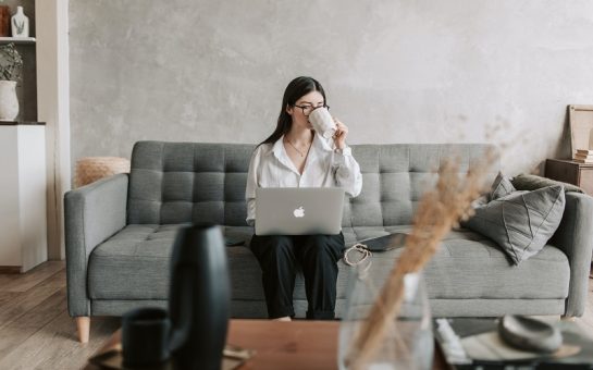 a woman working from her sofa sips coffee