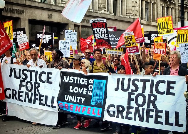 Anti-government protestors march on Whitehall in 2017. They carry placards reading "Justice for Grenfell", "Tories out". 