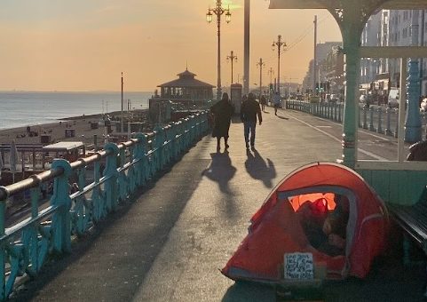 Local residents enjoy an evening stroll along the promenade as a homeless citizen sets up his tent for the night. Photo by Eve Salusbury