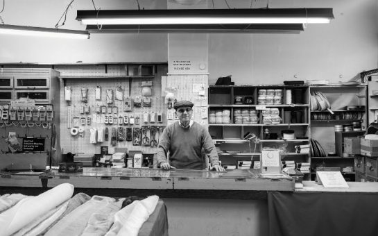 A black and white photo of Clapham shop owner Maurice Dorfman stood behind his shop counter.