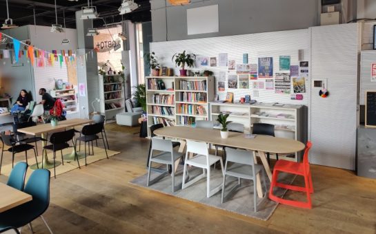 Landscape picture of London LGBT Community Centre's interior, showing a table and chairs and artwork around the walls