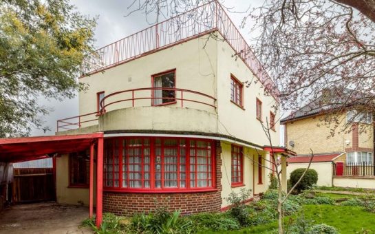 A detached house in the moderne style, designed by Leslie H Kemp and Frederick E Tasker and built by Cyril and Stanley Morrell 1935-1936. The house has external walls of rendered brick, with metal casement windows and a flat, concrete roof. The original house is rectangular on plan, with a projecting, curved bay to the south elevation at ground floor level. The front (east) elevation is at an oblique angle to the street while the adjacent garage to the north is perpendicular to the street. It retains several of its original features, including the bathroom fittings, iron staircase, Crittall windows and a roof terrace. At ground-floor level the semi-circular bay has exposed red brick laid in Flemish bond and a continuous, curved window. General view of exterior from south east.