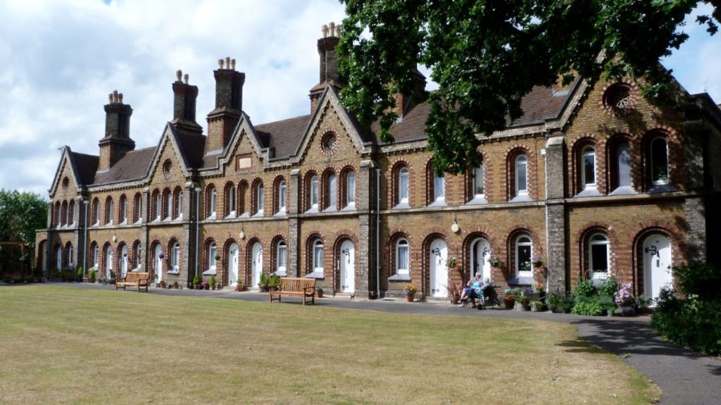 A picture of the front of Church Estate Almshouses in Richmond owned by the Richmond Charities, with two benches and a garden outside the housing.